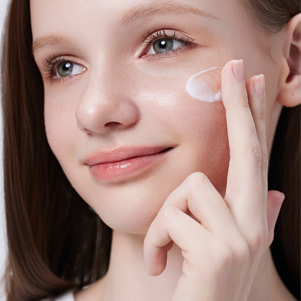 Une femme applique la crème hydratante COSRX The Ceramide Skin Barrier sur sa joue.