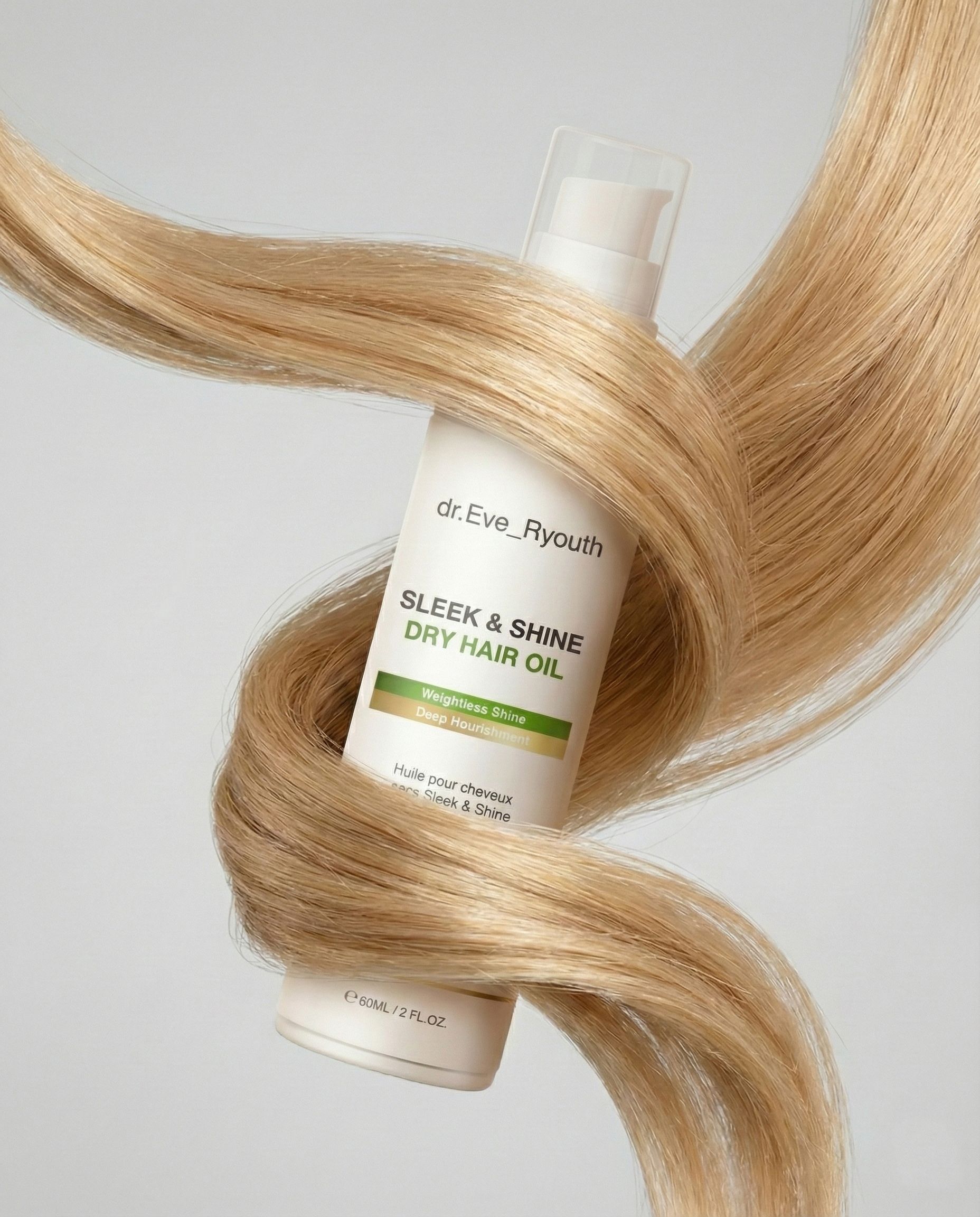 Une bouteille d'huile sèche Sleek & Shine est entourée de longs cheveux blonds.