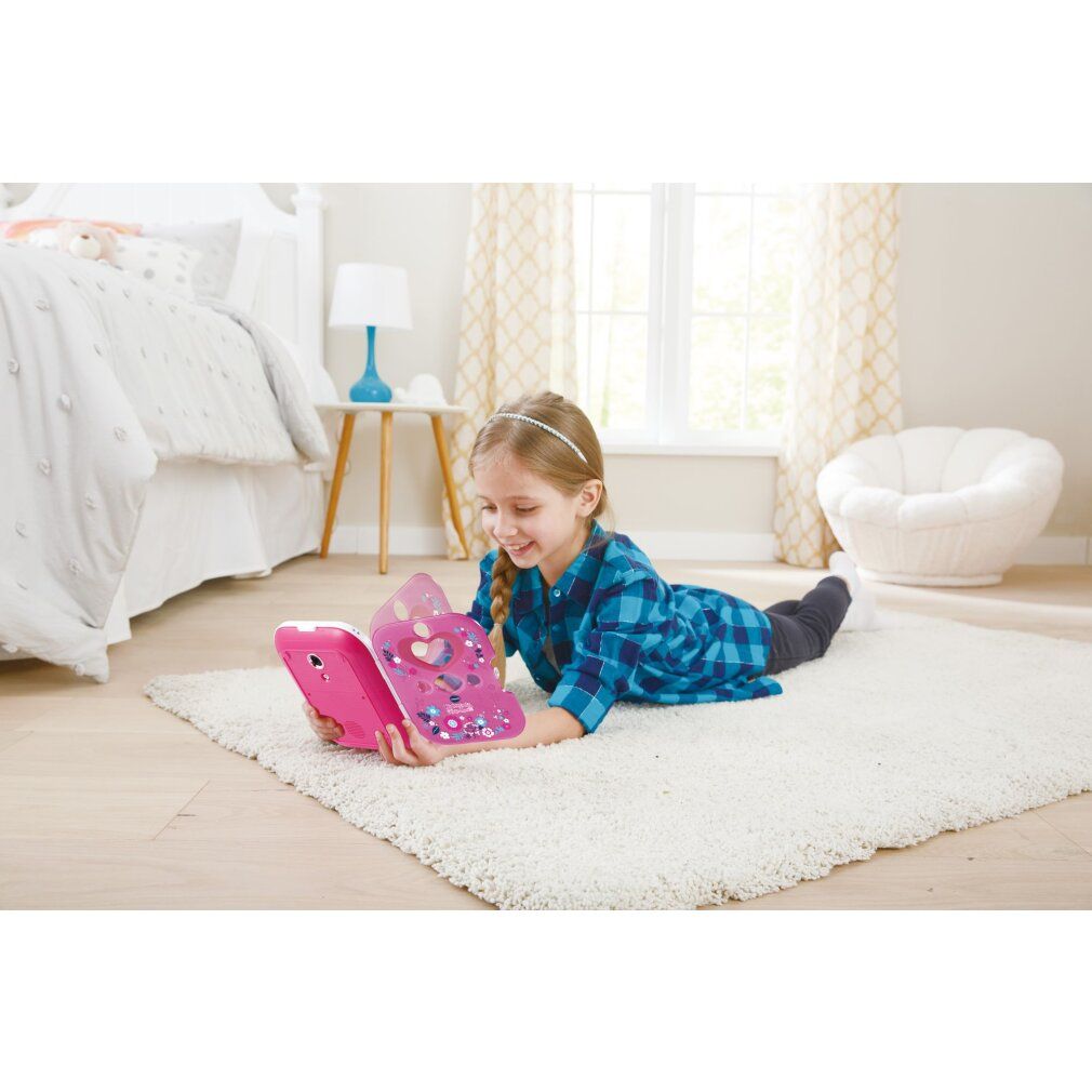 Une fille allongée sur un tapis utilise un journal VTech Kidisecrets Selfie Music 2.0 rose.