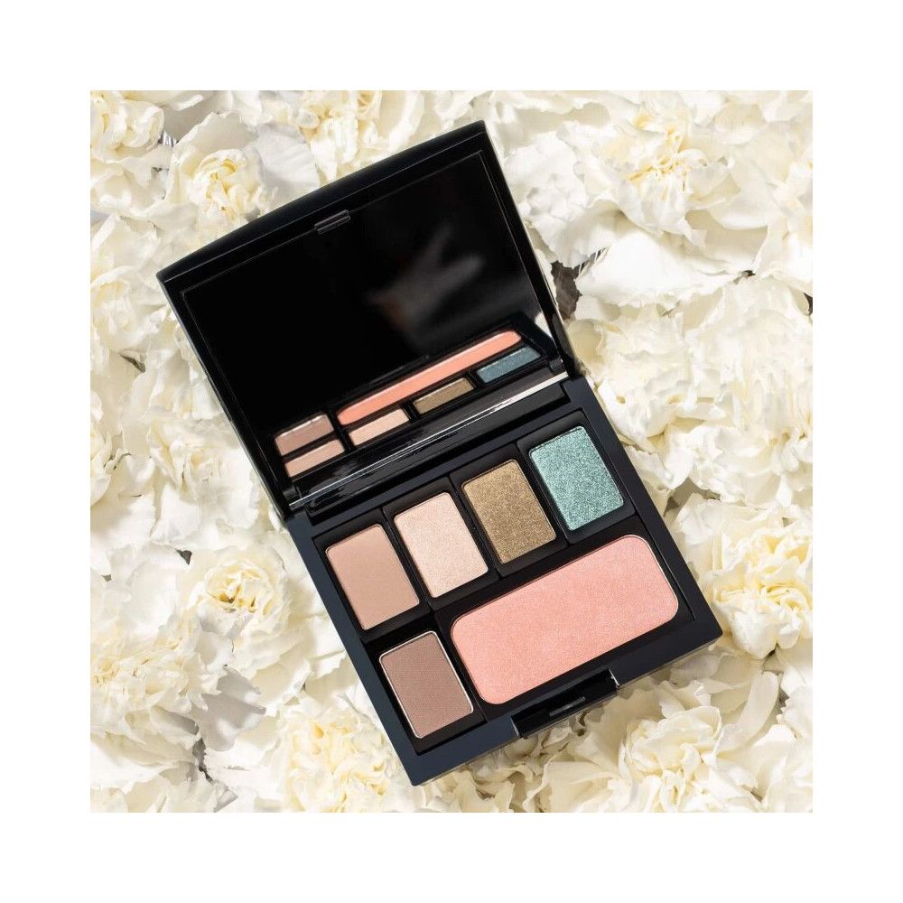 Beauty Box noire ouverte avec différents fards à paupières et blush, sur des fleurs blanches.