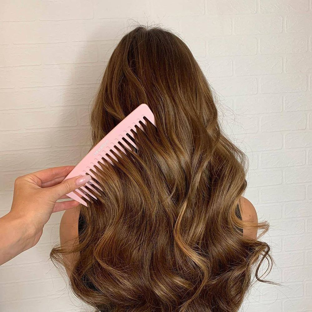 Un peigne rose pâle à larges dents utilisé dans de longs cheveux ondulés.
