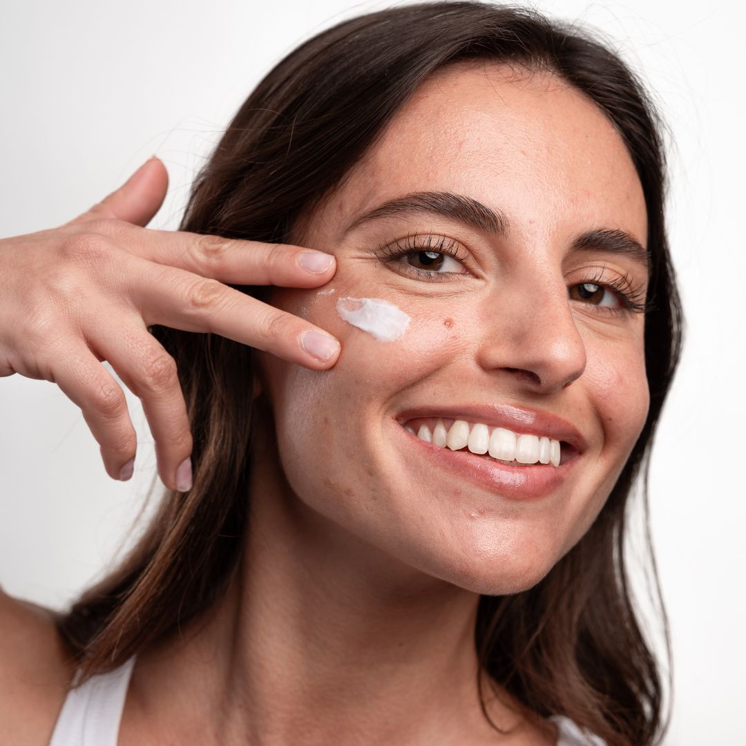 Femme appliquant de la crème sur son visage. Crème blanche sur la peau. Elle sourit.