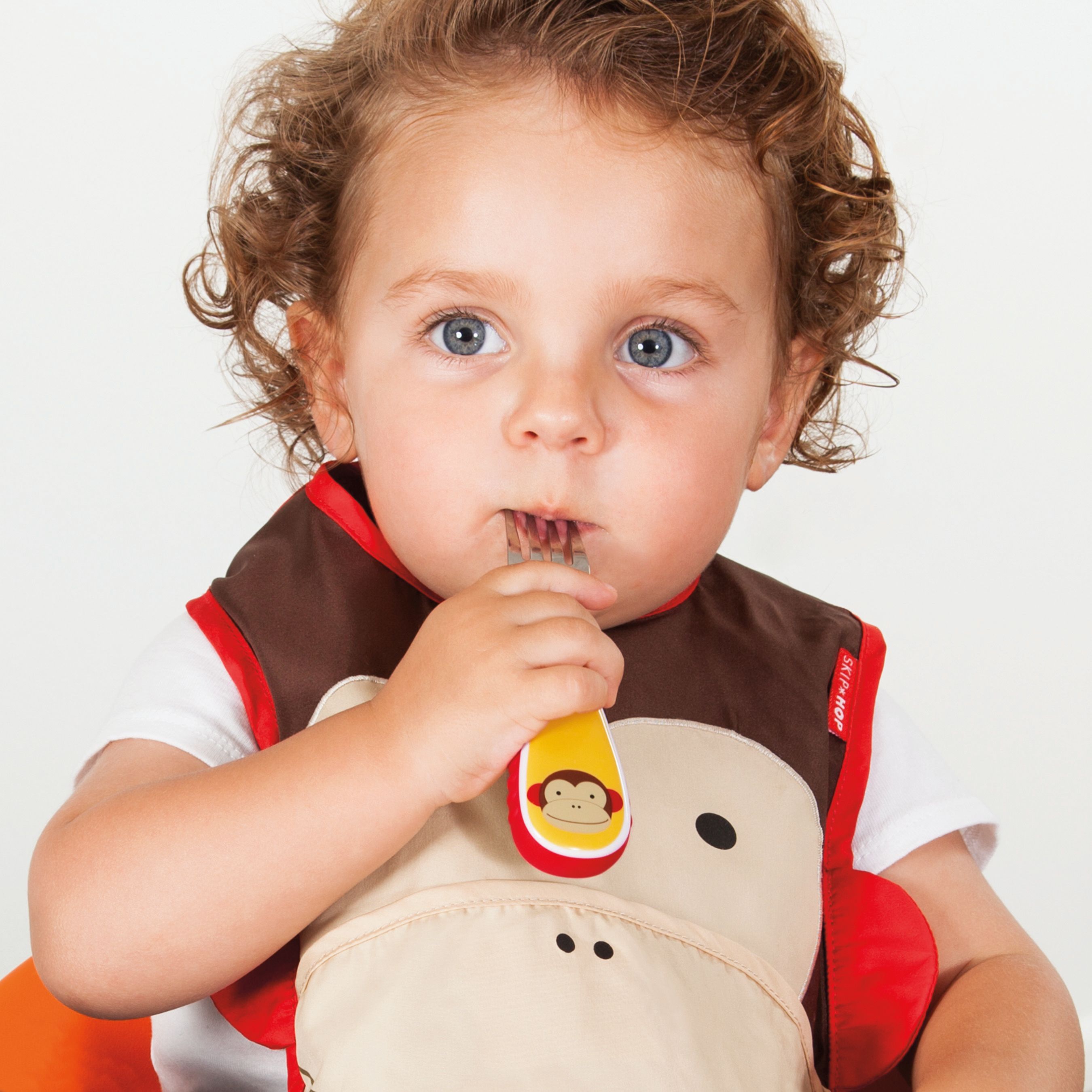 Peuter met lepel in de mond. Het kind draagt een slabbetje met apenmotief.