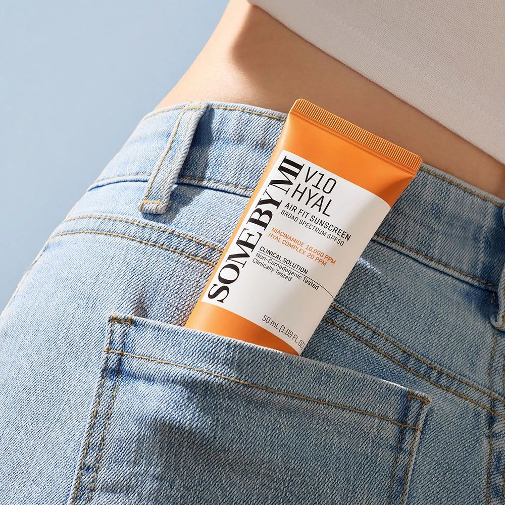 Tube de crème solaire dans une poche arrière de jean. Tube orange et blanc avec texte : SOME BY MI V10 Hyal Air Fit Sunscreen SPF50.