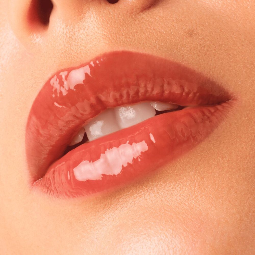 Close-up van lippen met glanzende lipgloss. Kleur: oranje-bruin. Lippen zijn licht geopend.