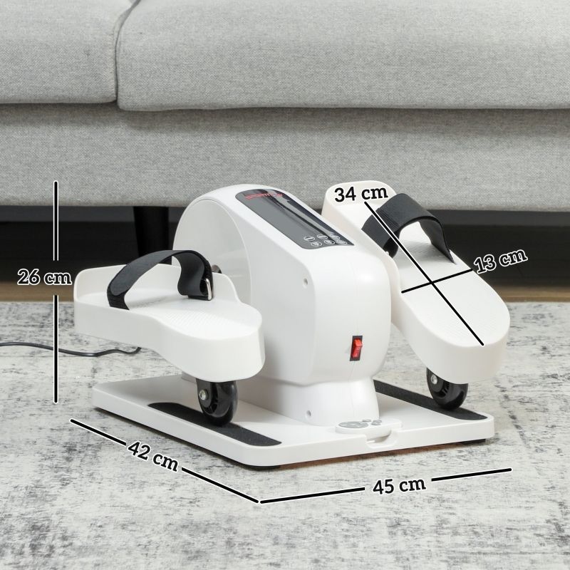 Witte mini-elliptische trainer met zwarte banden, afmetingen 45x42x26 cm. Rode aan/uit-knop, wielen. Op tapijt voor bank.