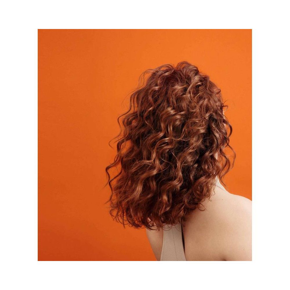 Vue arrière d'une personne aux cheveux roux bouclés. Fond orange.