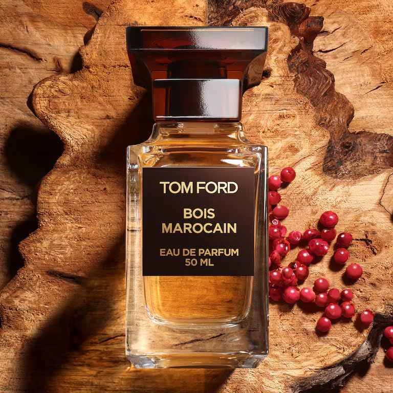 Glazen fles met bruine dop. Opschrift: TOM FORD, BOIS MAROCAIN, EAU DE PARFUM, 50 ML. Achtergrond: hout en rode bessen.