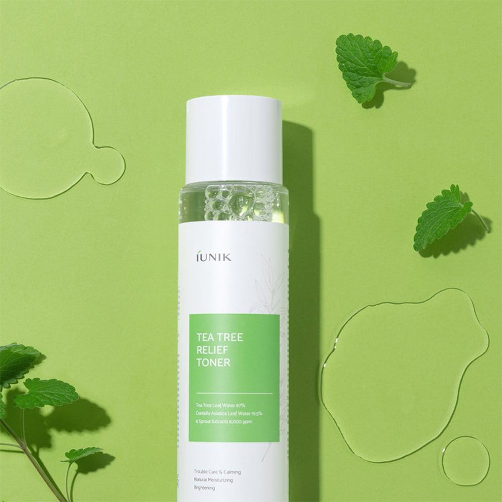 iUNIK Tea Tree Relief Toner sur fond vert avec des gouttes d'eau et des feuilles. Bouteille transparente avec bouchon blanc.