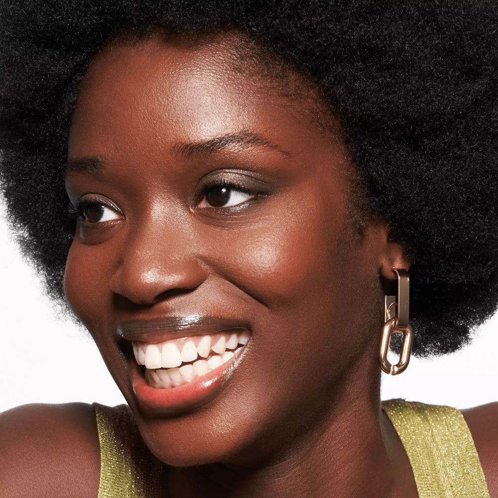 Femme à la peau foncée, souriante. Baume à lèvres appliqué.