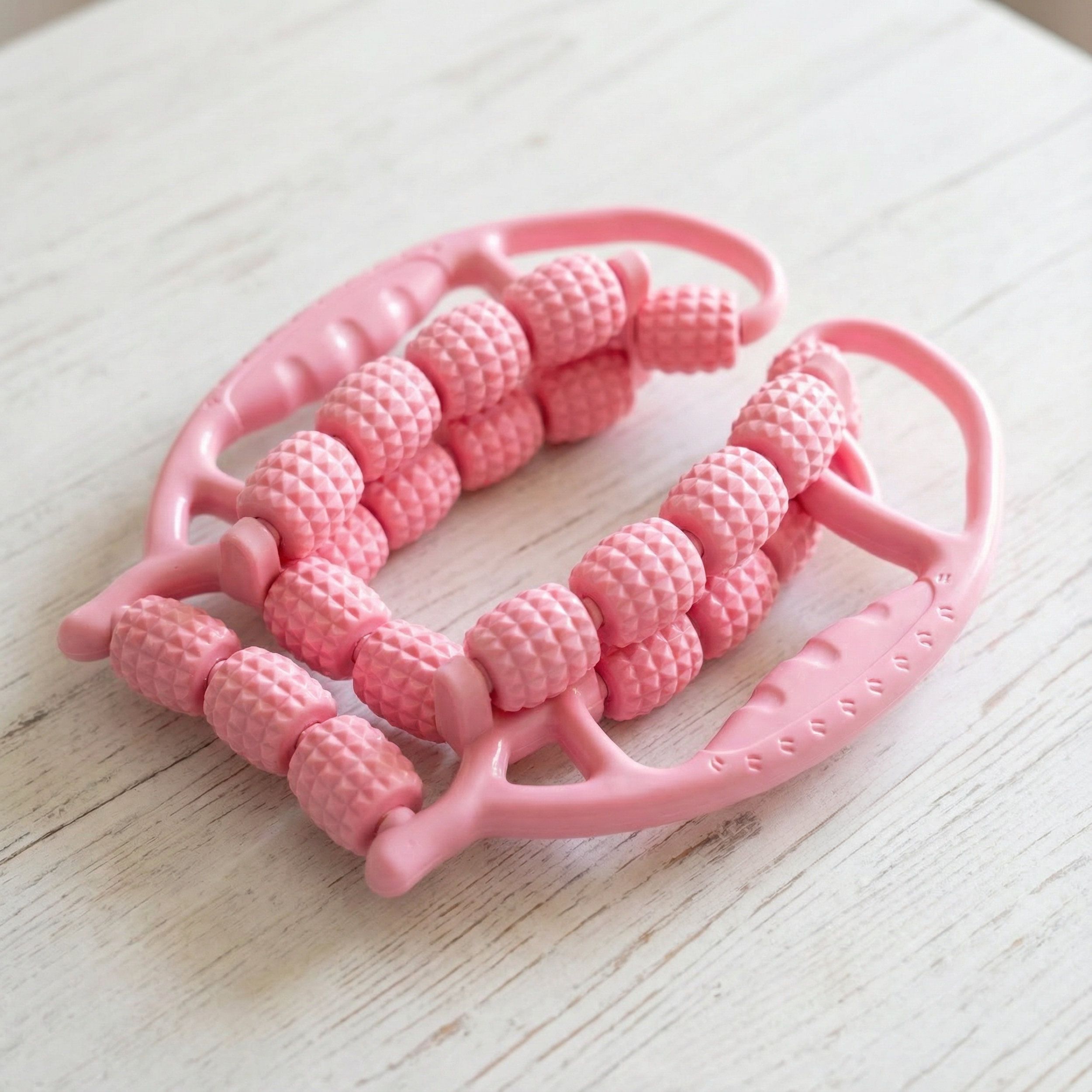Roze massageroller, close-up. Meerdere rollen met handvatten. Op lichte houten ondergrond.