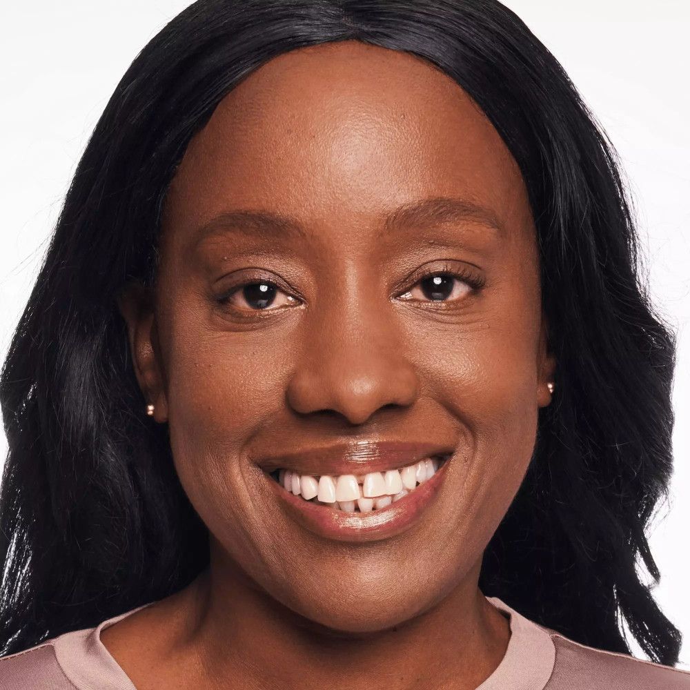 Portret van een vrouw met een donkere huid. Ze lacht. Ze draagt oorbellen.