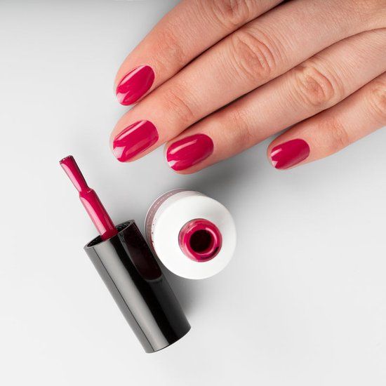 Main avec ongles vernis Festive Fuchsia. Flacon de vernis et pinceau à côté. Pinceau dans le flacon.