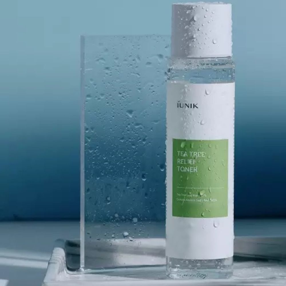 Tonerfles met witte dop, druppels. Groen etiket met tekst: iUNIK, Tea Tree Relief Toner. Op dienblad.