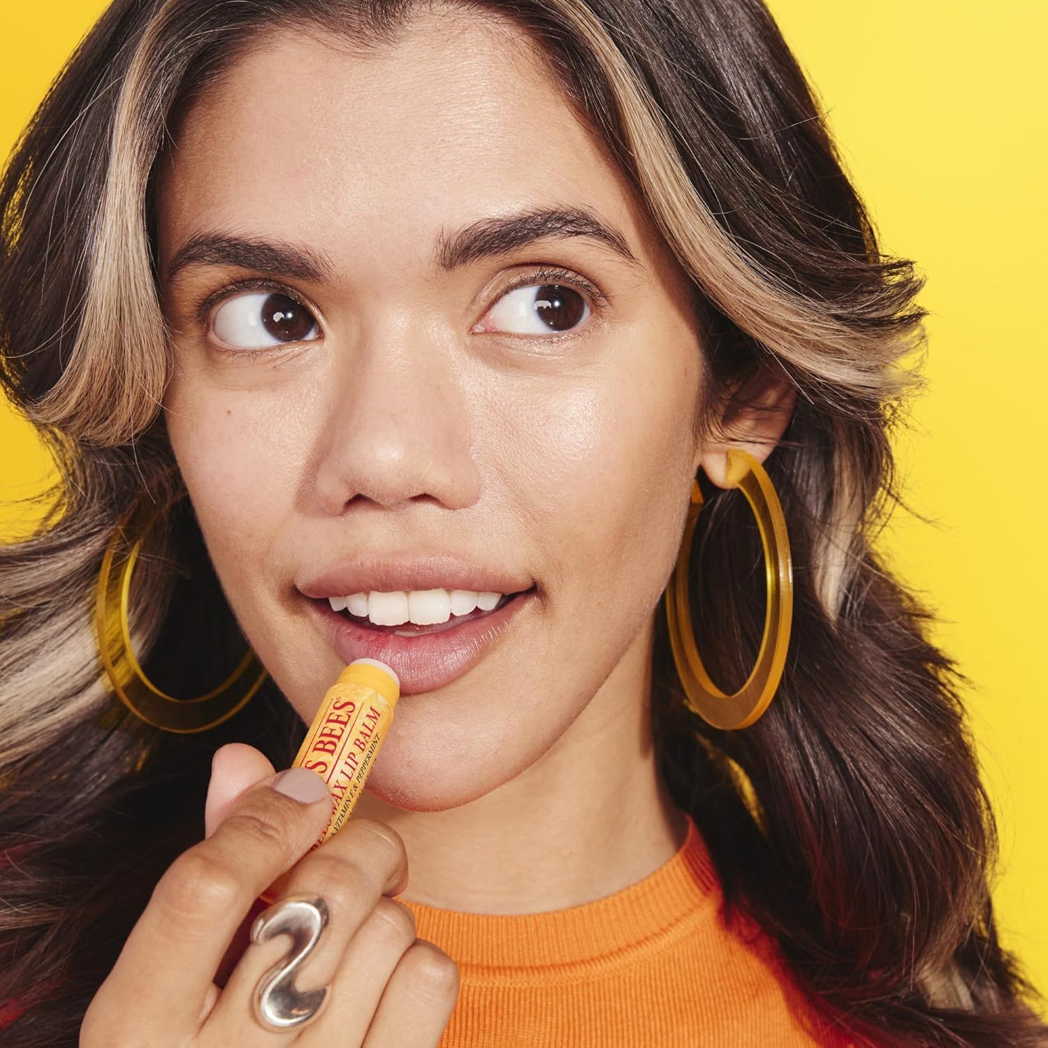 Une femme applique du baume à lèvres Burt's Bees. Le baume est dans un tube jaune.