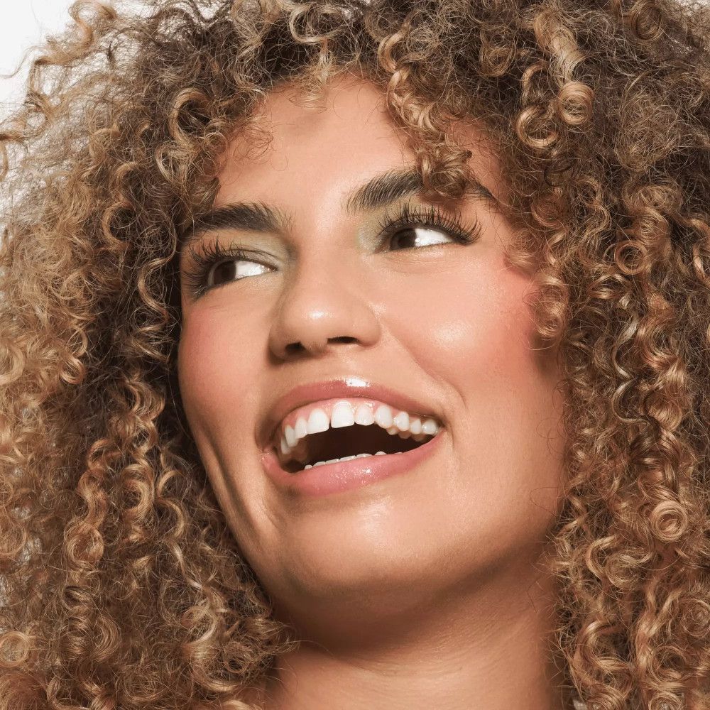 Femme aux cheveux bouclés, souriante. Baume à lèvres appliqué.