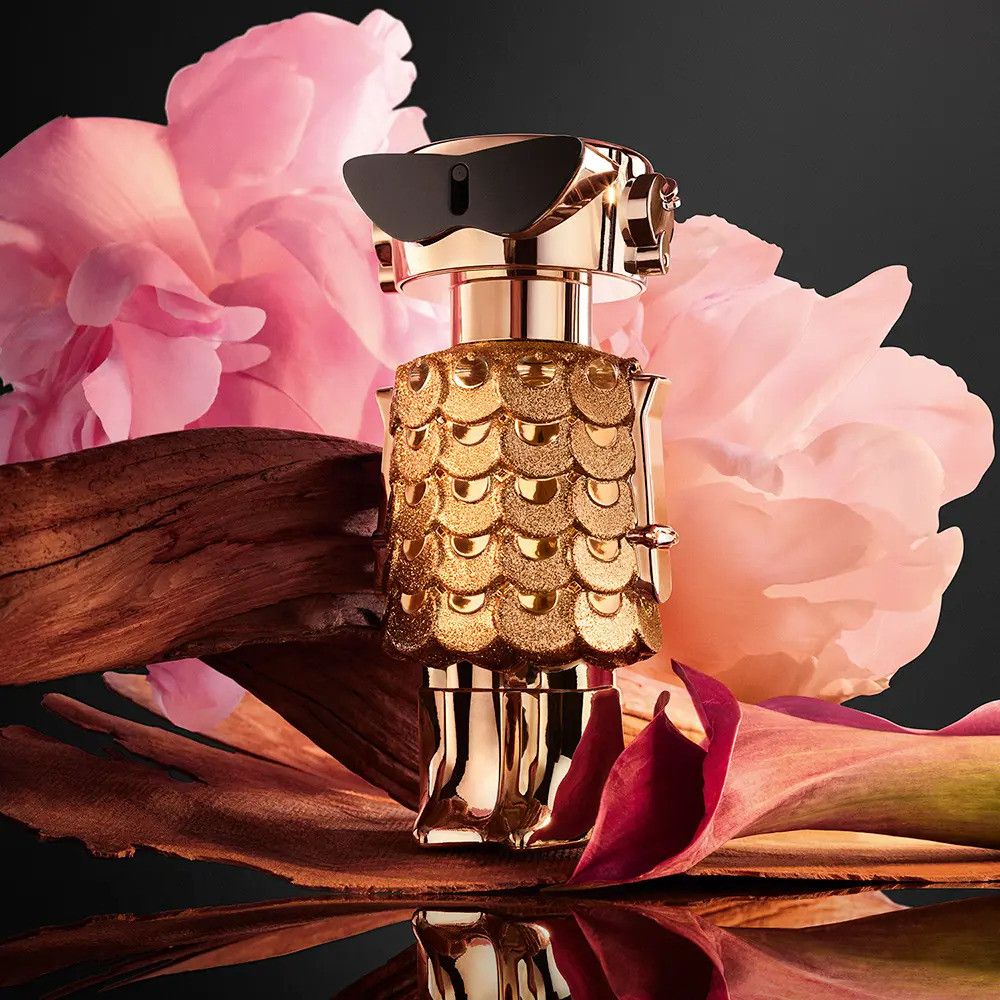 Gouden fles met zwarte zonnebril, omringd door bloemen en hout. Flesontwerp: robot.