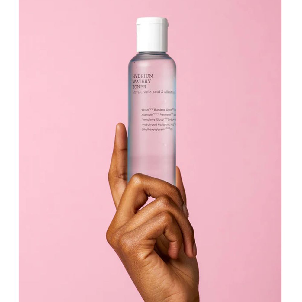 Transparante tonerfles in een hand. Opschrift: Hydrium Watery Toner. Ingrediënten zichtbaar.