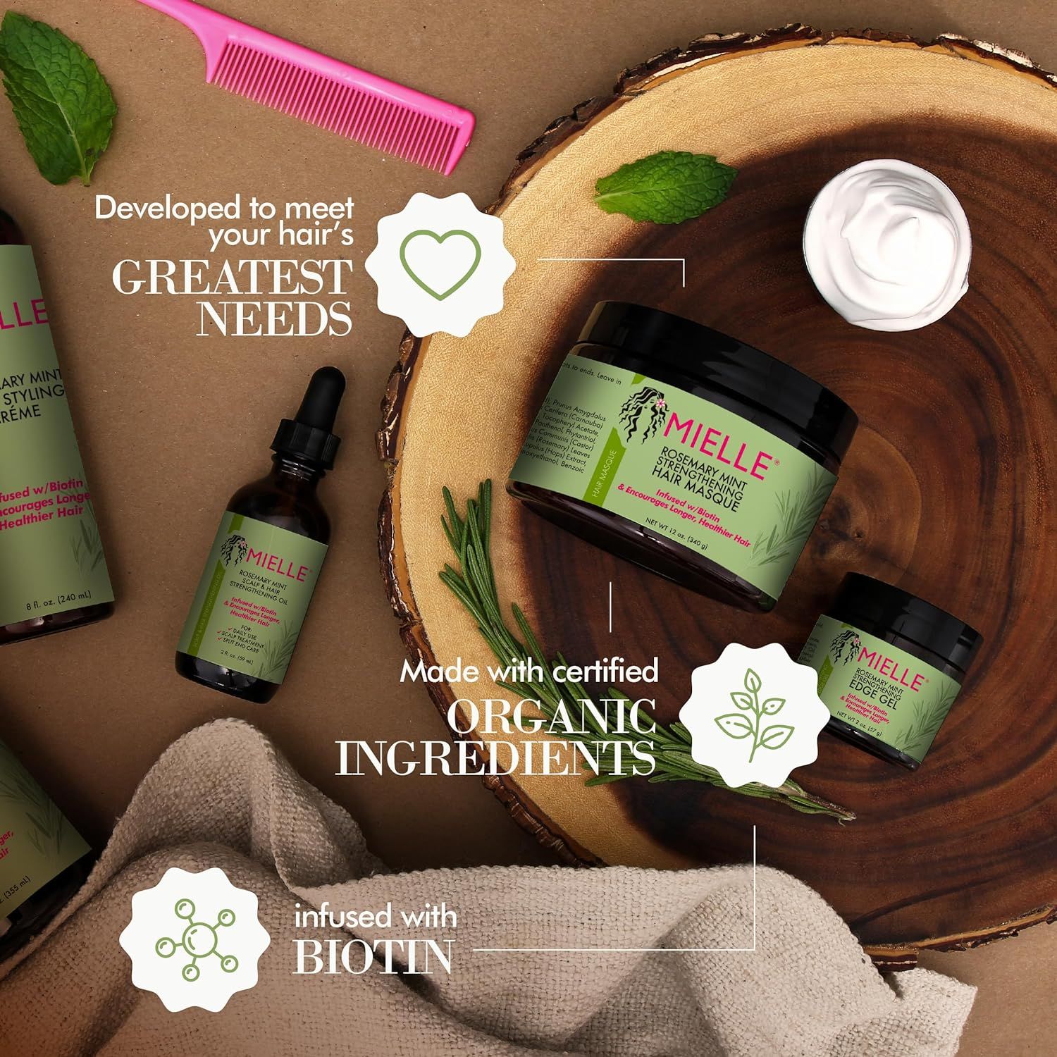 Mielle Rosemary Mint producten, verrijkt met biotine, op een houten ondergrond met rozemarijn en munt.