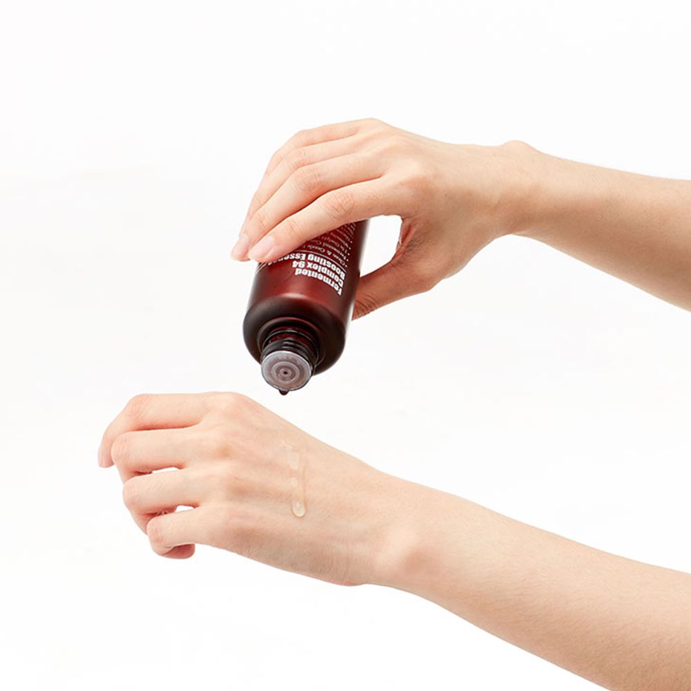 Handen houden een bruine fles vast. Vloeistof druppelt op de handpalm. Fles met zwarte dop.