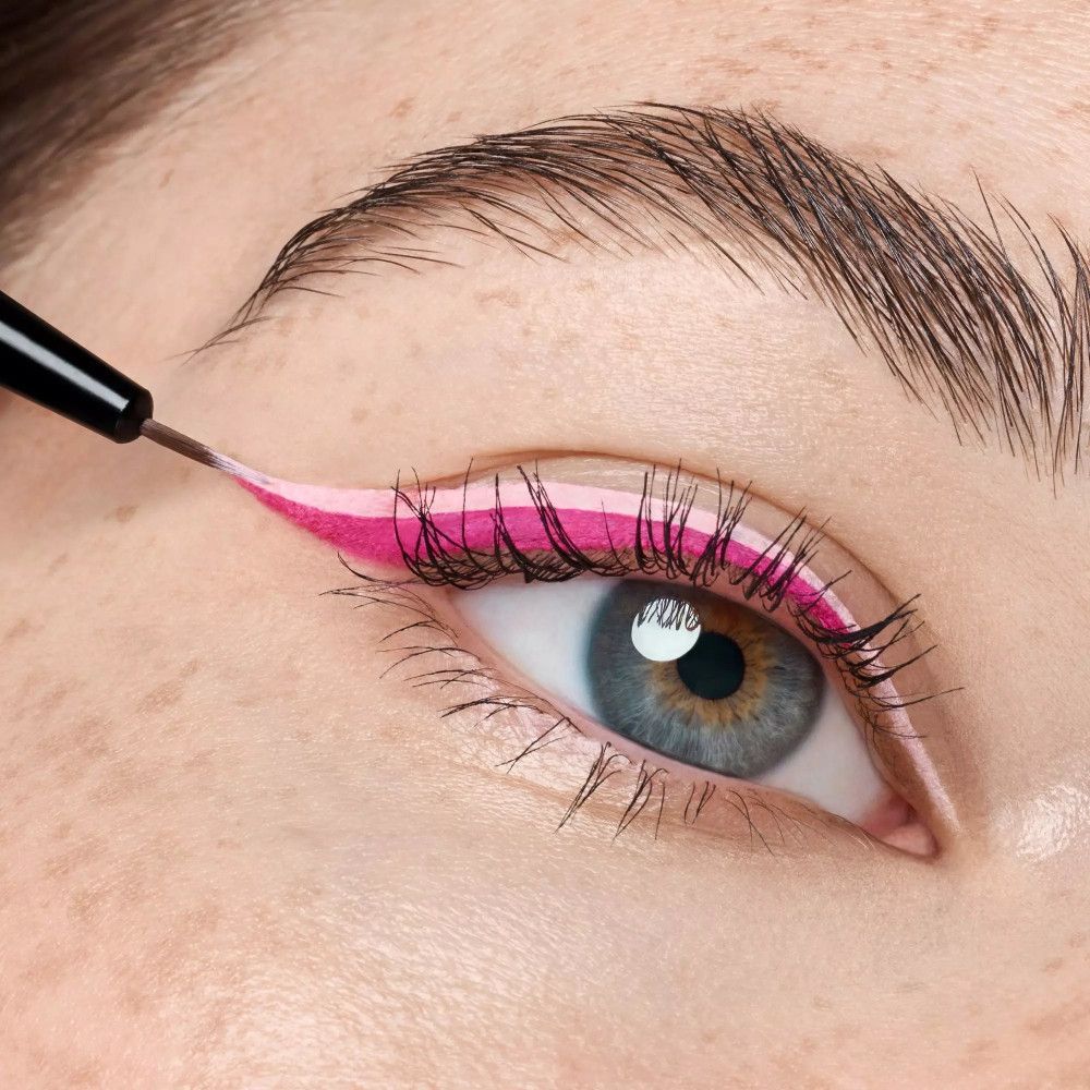 Gros plan sur un œil maquillé avec un pinceau eyeliner. Pinceau en main, traçant une ligne.