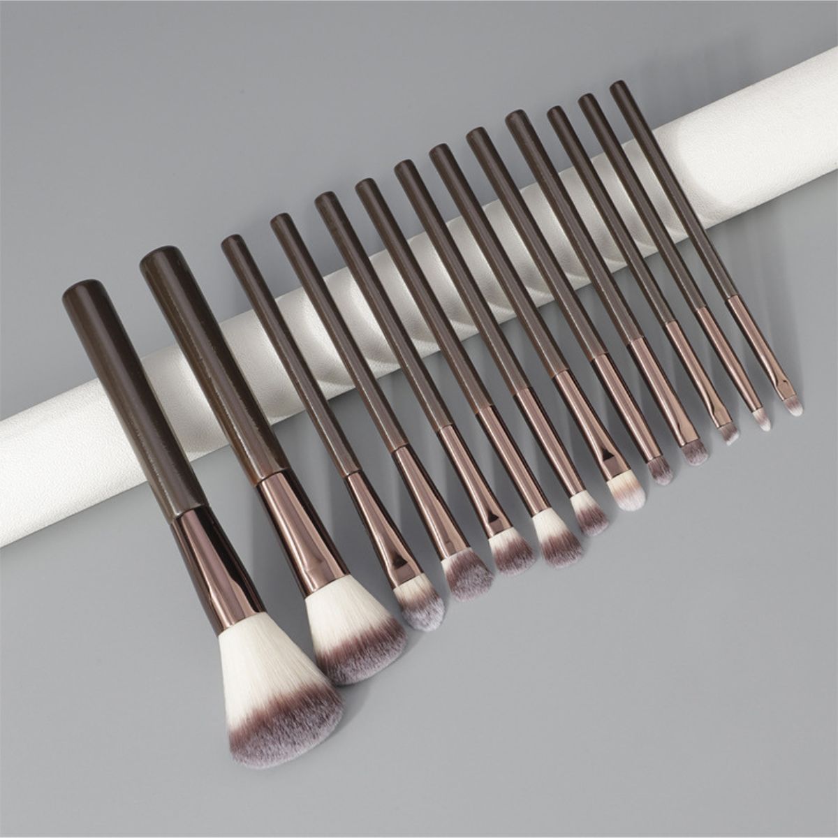 Un ensemble de 12 pinceaux de maquillage foncés avec des viroles argentées et des poils duveteux.