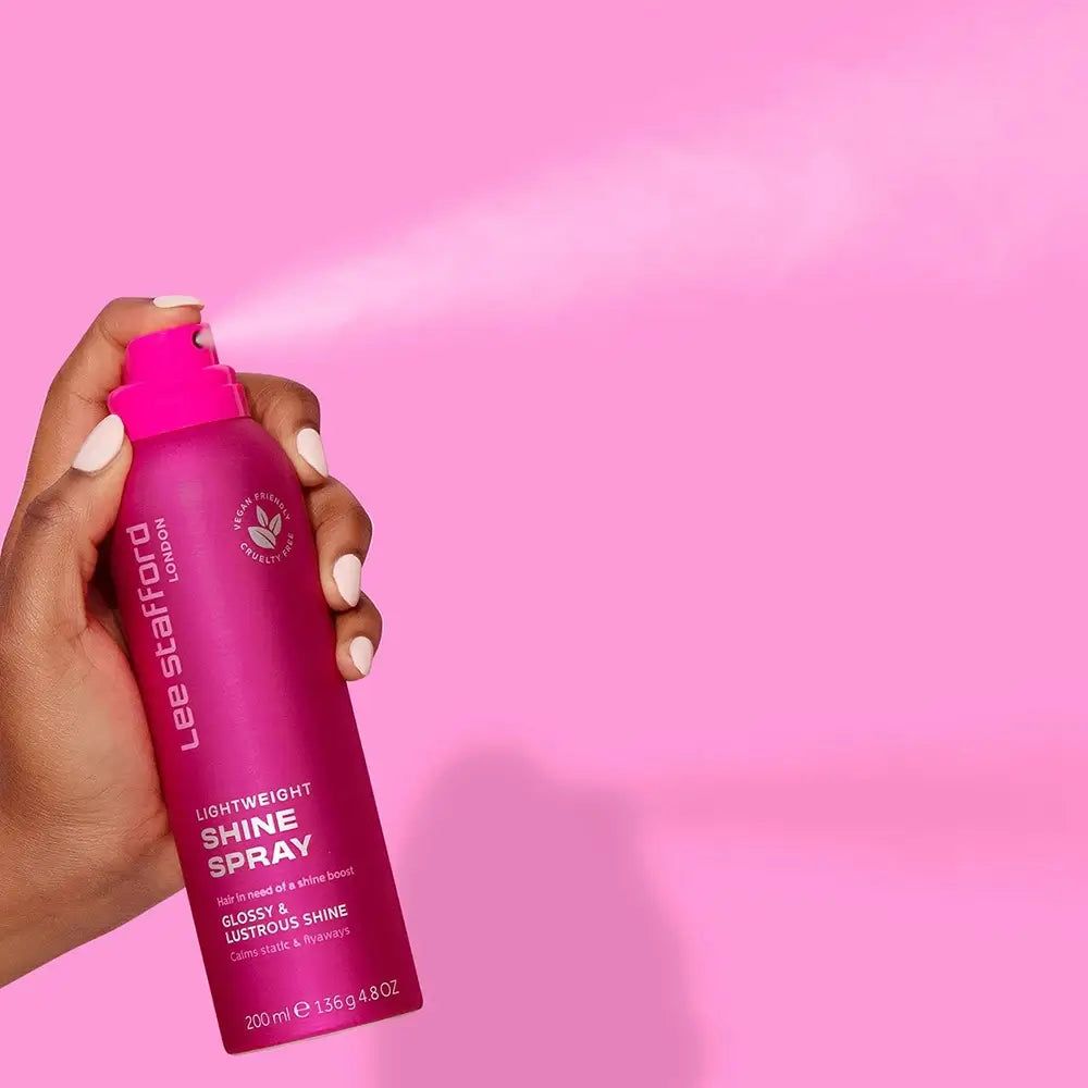 Main pulvérisant le spray brillance légère Lee Stafford d'un flacon rose.