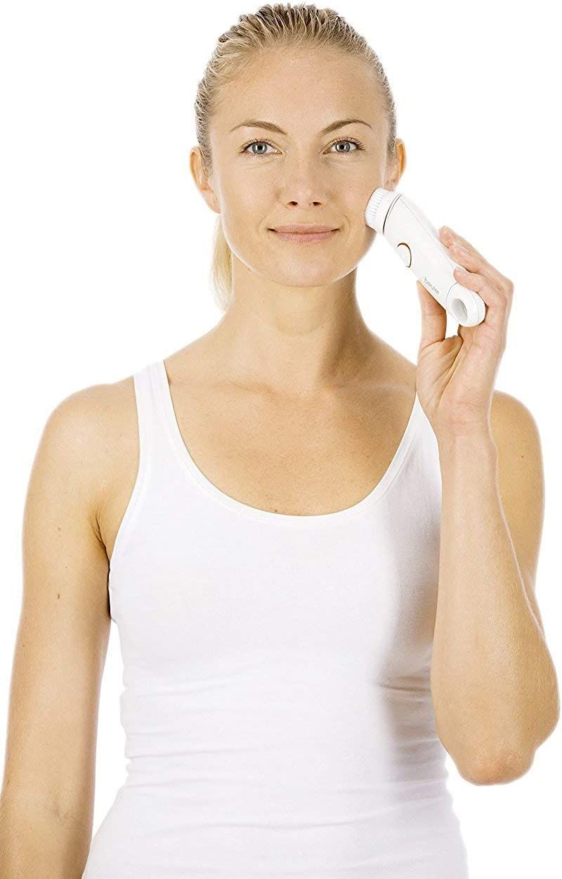 Vrouw houdt gezichtsborstel vast. Wit apparaat met roze knop en borstelkop. Gebruik.