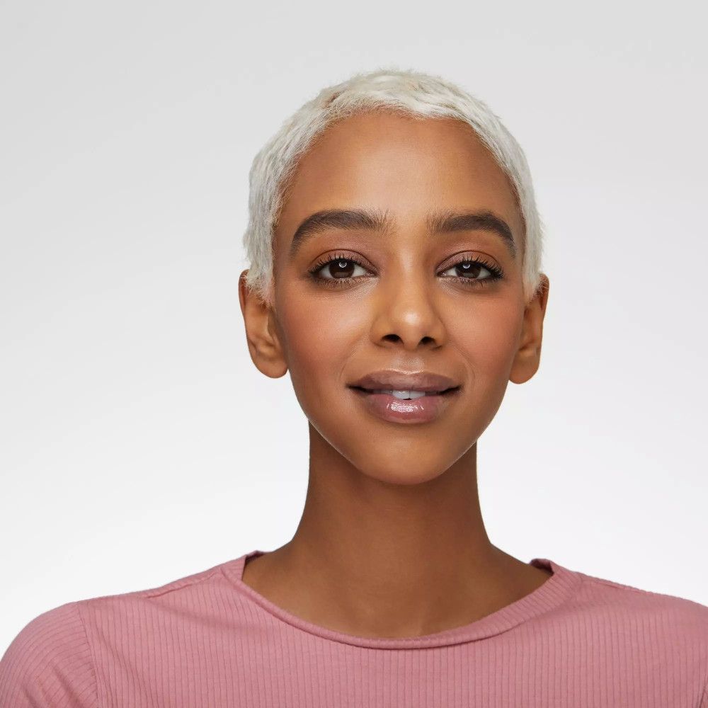 Portret van een vrouw met een roze top. Ze draagt lipgloss. Lichte huid, kort blond haar.