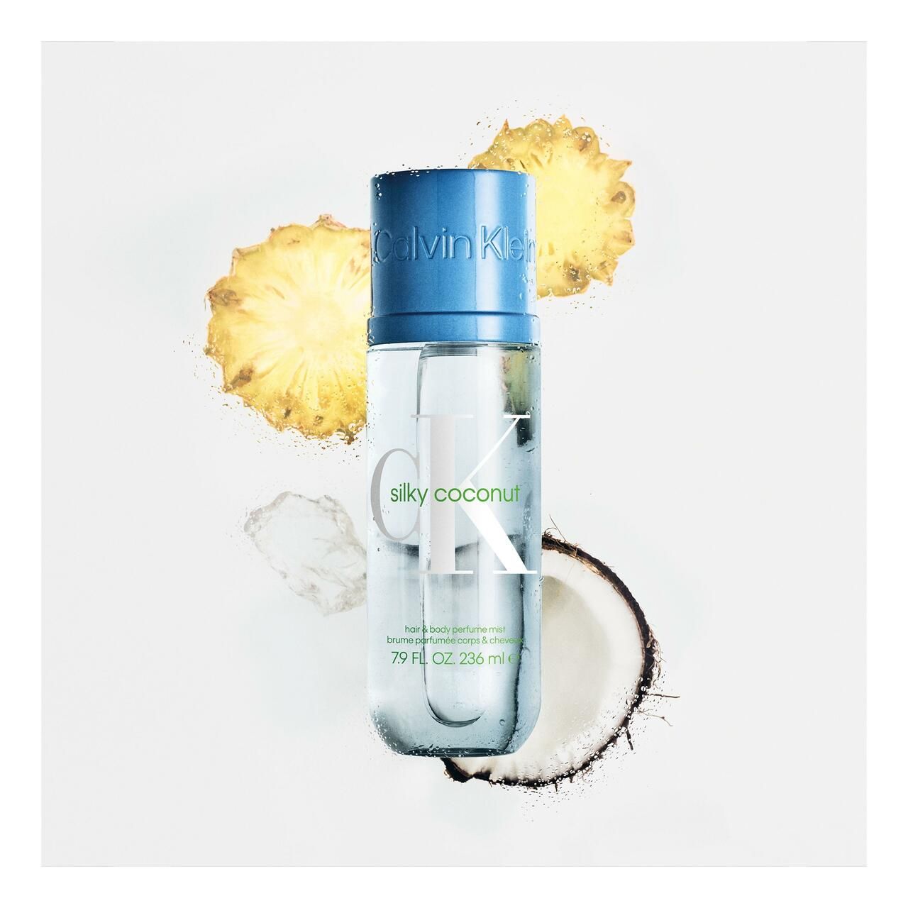 Flacon transparent avec bouchon bleu. Inscription: Calvin Klein, Silky Coconut. Morceaux de noix de coco et d'ananas en arrière-plan.