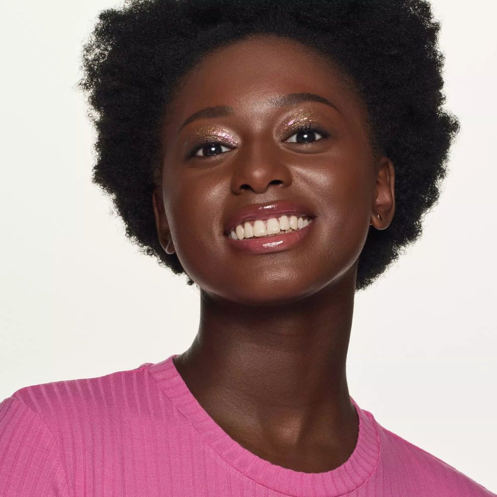 Portret van een vrouw met gebruinde huid en roze lippen. Ze draagt een roze top en lacht.