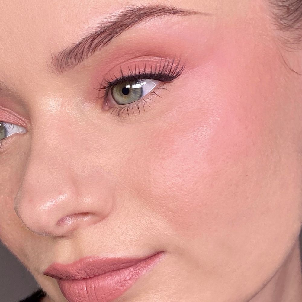 Gros plan d'un visage maquillé de rose sur les yeux et les joues. Yeux verts, faux cils.