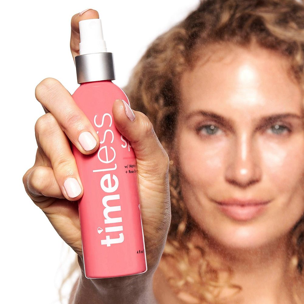 Vrouw houdt roze sprayfles vast. Opschrift: timeless, HA Spray, Matrixyl 3000, Rose Extract. 4 fl oz (120 ml).