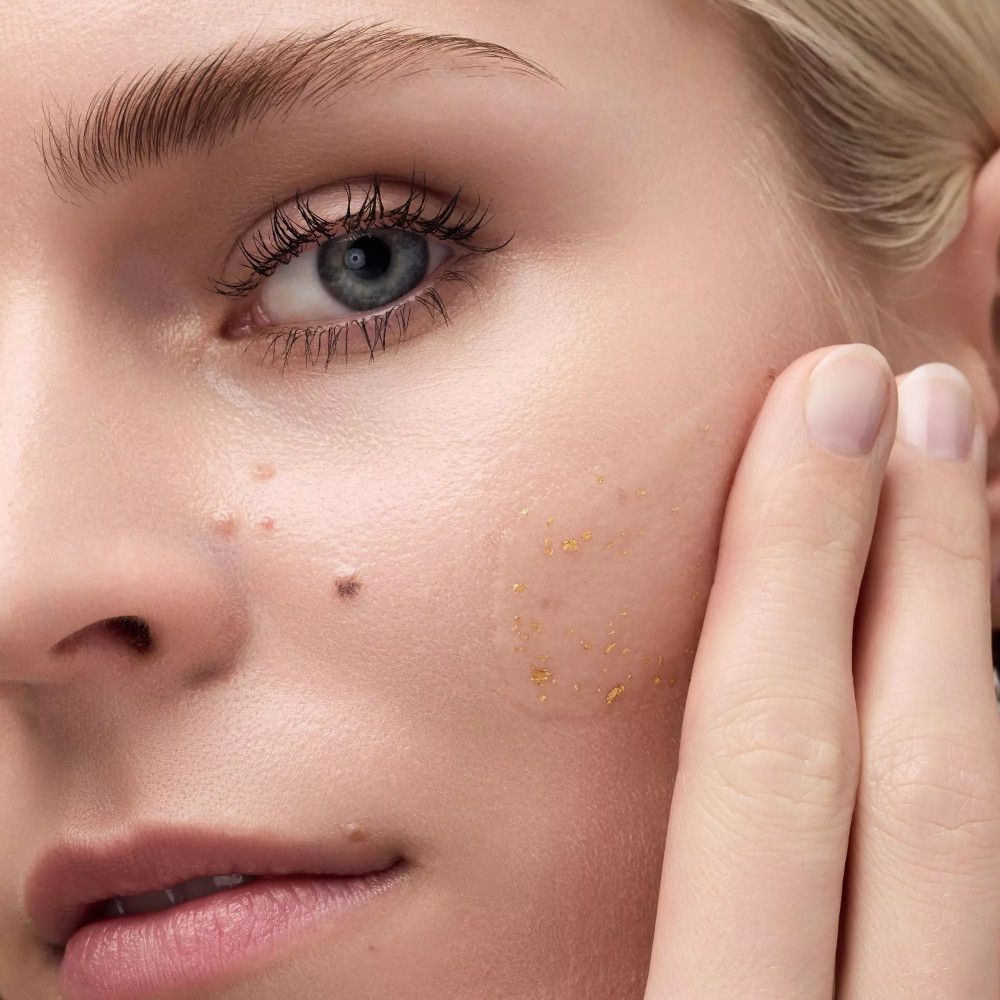 Gros plan d'un visage. Produit appliqué avec des particules dorées sur la peau. Doigt touchant la peau.