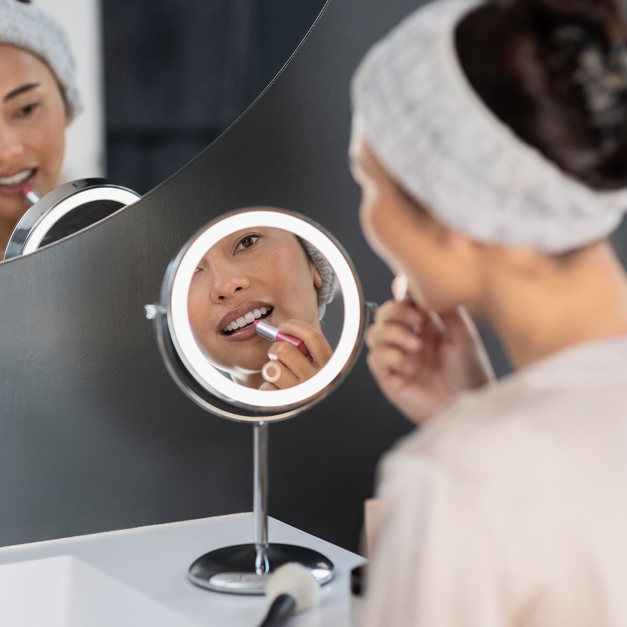 Femme utilisant un miroir cosmétique avec éclairage LED. Le miroir reflète le visage. Miroir monté au mur.