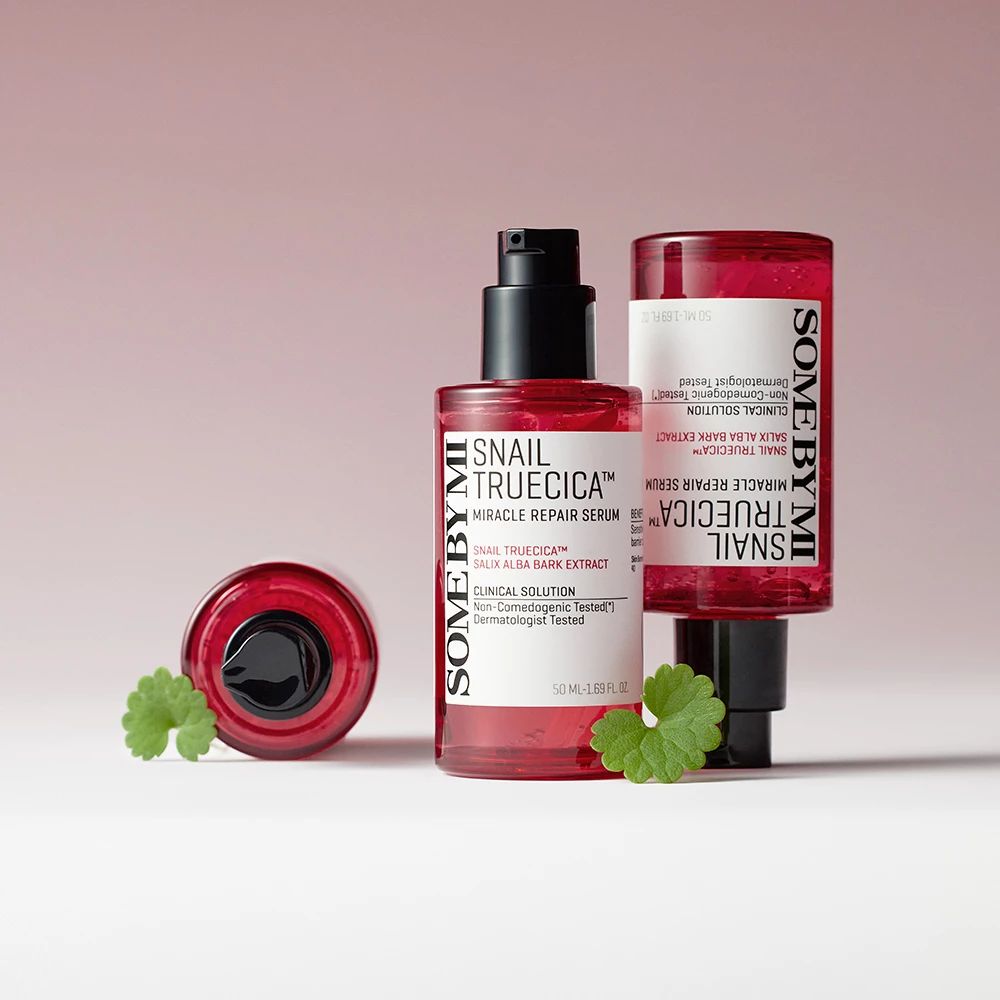 Twee serumflessen met zwarte pomp en een dop. Productlabels zichtbaar. Groene bladeren ernaast.