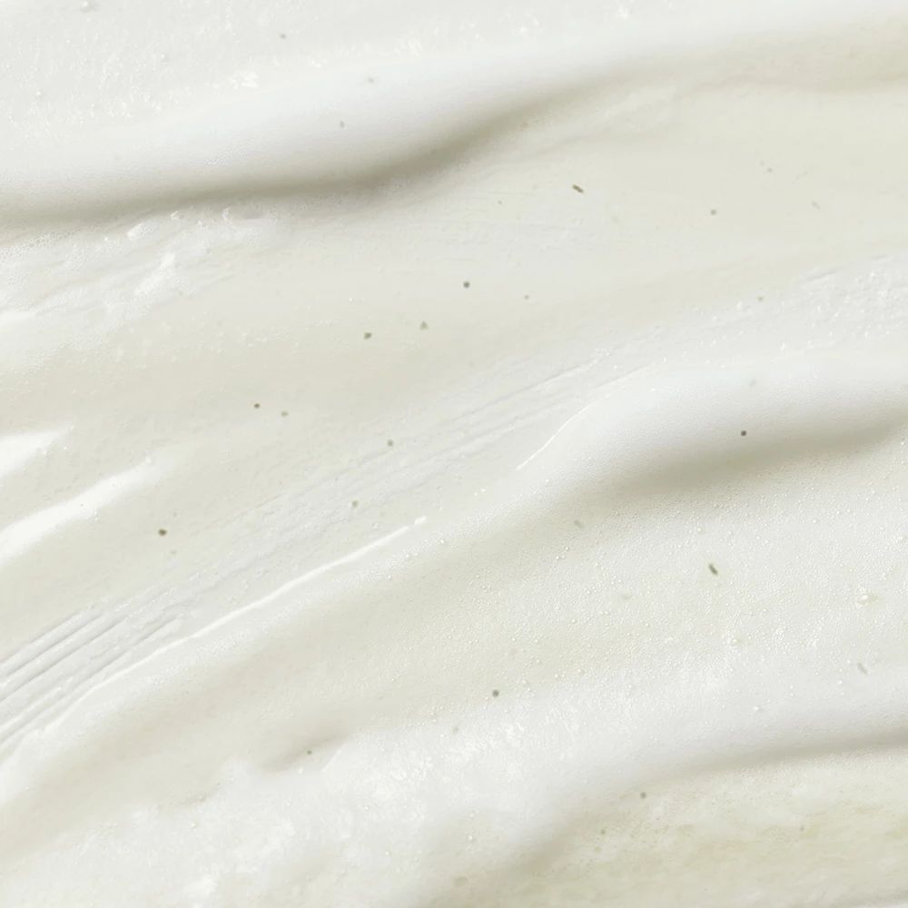 Close-up van witte, romige substantie. Kleine groene deeltjes zichtbaar. Textuur is glad.