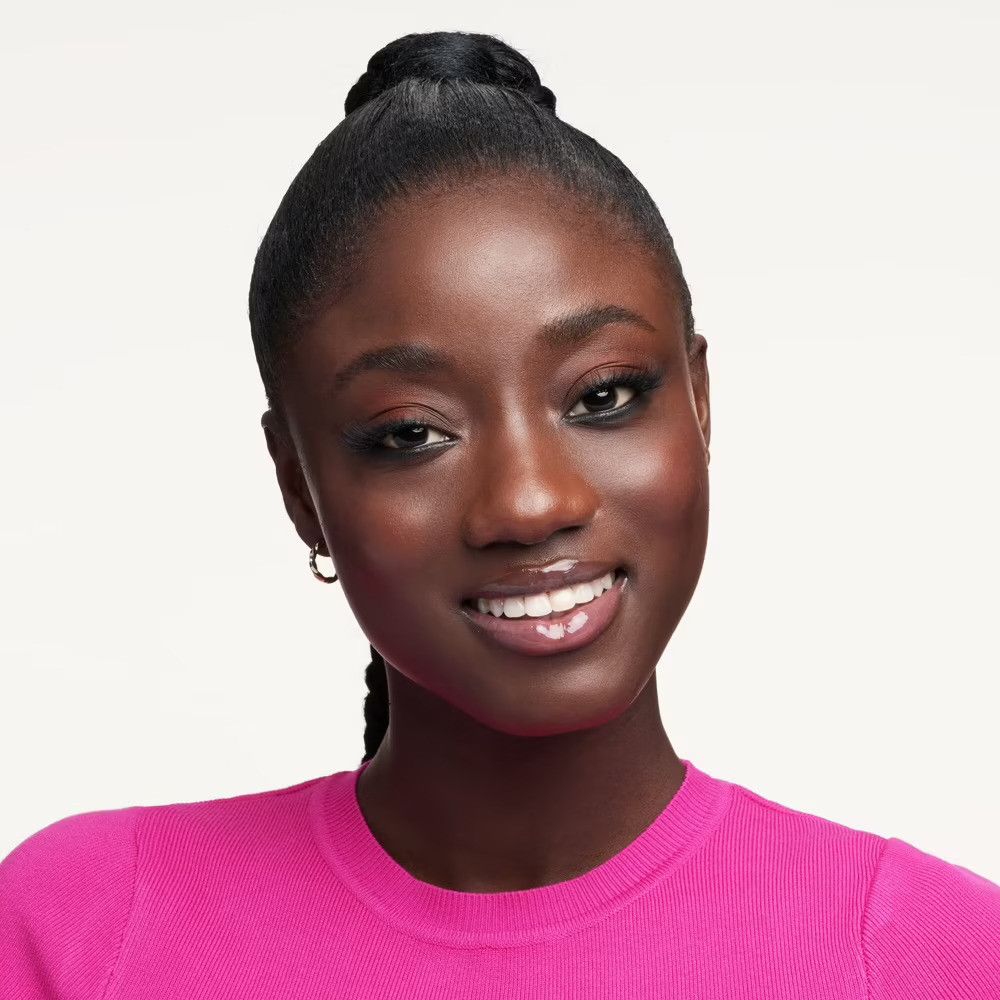 Portrait d'une femme souriante à la peau foncée et aux cheveux attachés. Elle porte un haut rose.