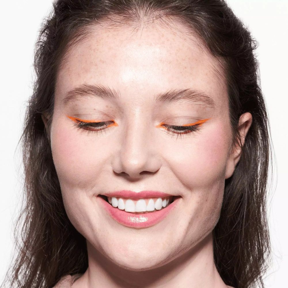 Femme avec trait de khôl sur les paupières. Elle sourit et porte du rouge à lèvres rosé.