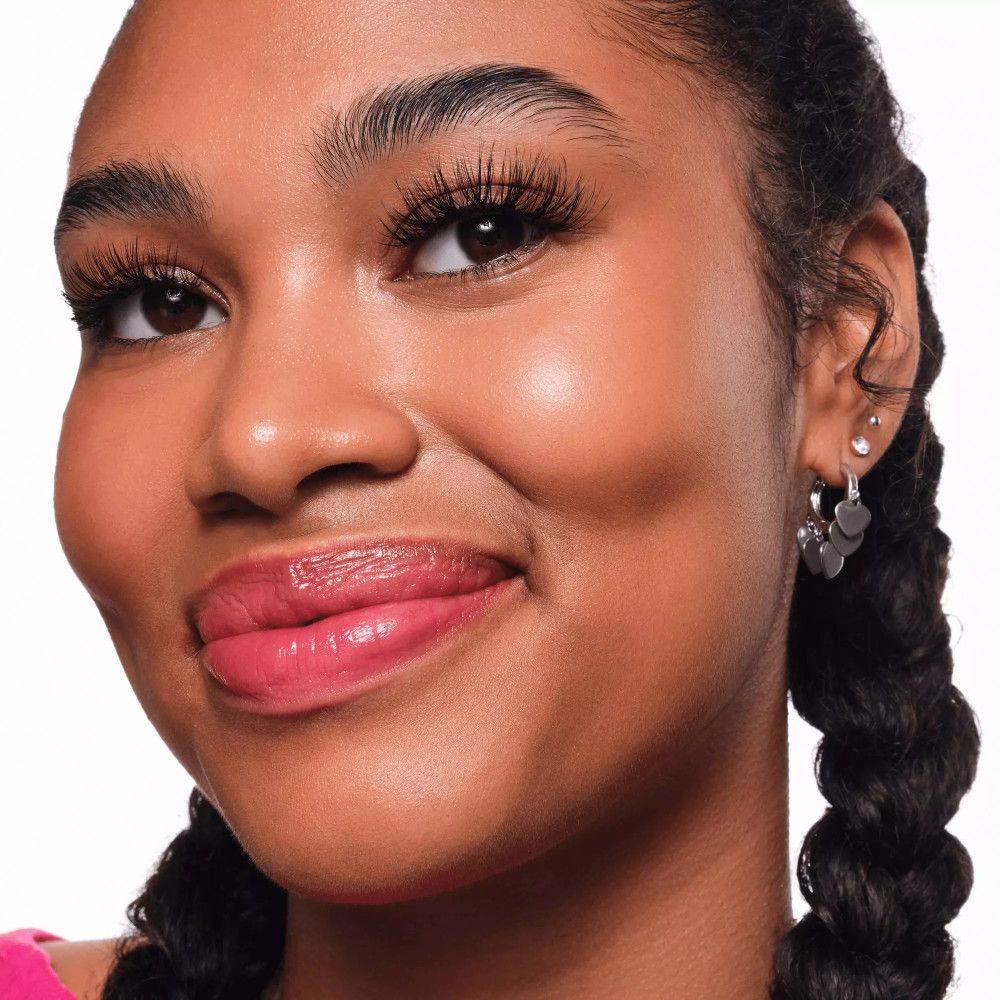 Portrait d'une personne portant de faux cils. La personne sourit et porte des boucles d'oreilles.