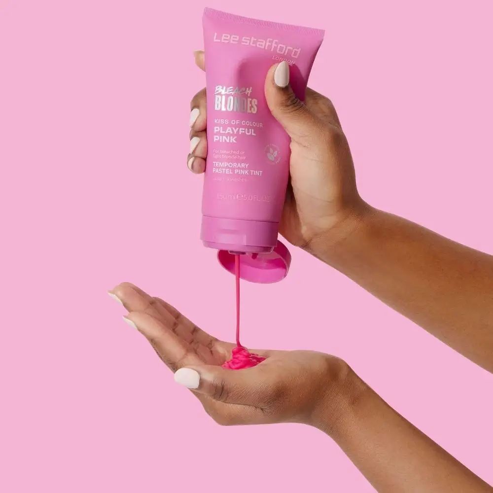 Handen houden roze tube vast. Product wordt in handpalm gedrukt. Roze vloeistof stroomt eruit. Roze achtergrond.