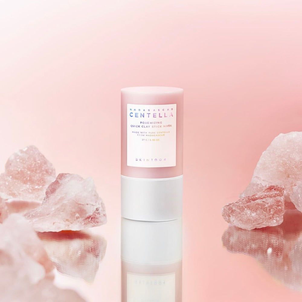 Roze cilindrisch gezichtsmasker, omringd door roze kristallen. Tekst: Madagascar Centella, Poremizing Quick Clay Stick Mask.