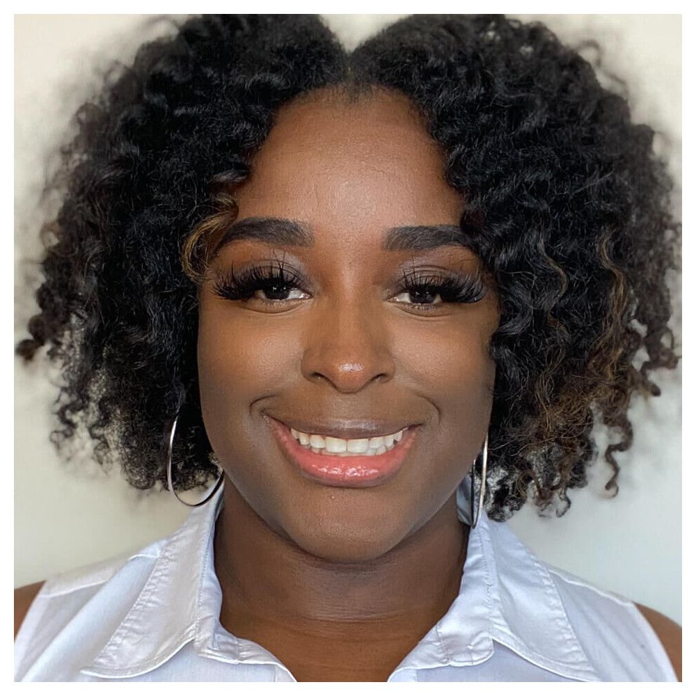 Portrait d'une femme souriante aux cheveux bouclés. Elle porte des boucles d'oreilles.