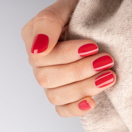 Main avec ongles vernis rouge framboise. Quelques ongles avec des rayures blanches. Pull couleur chair.
