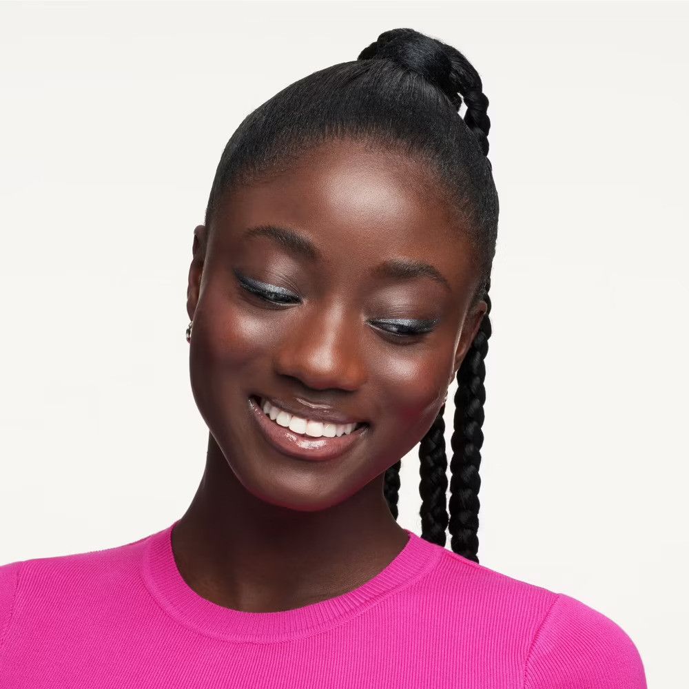 Portrait d'une femme souriante avec des tresses. Elle porte un haut rose et regarde vers le bas.
