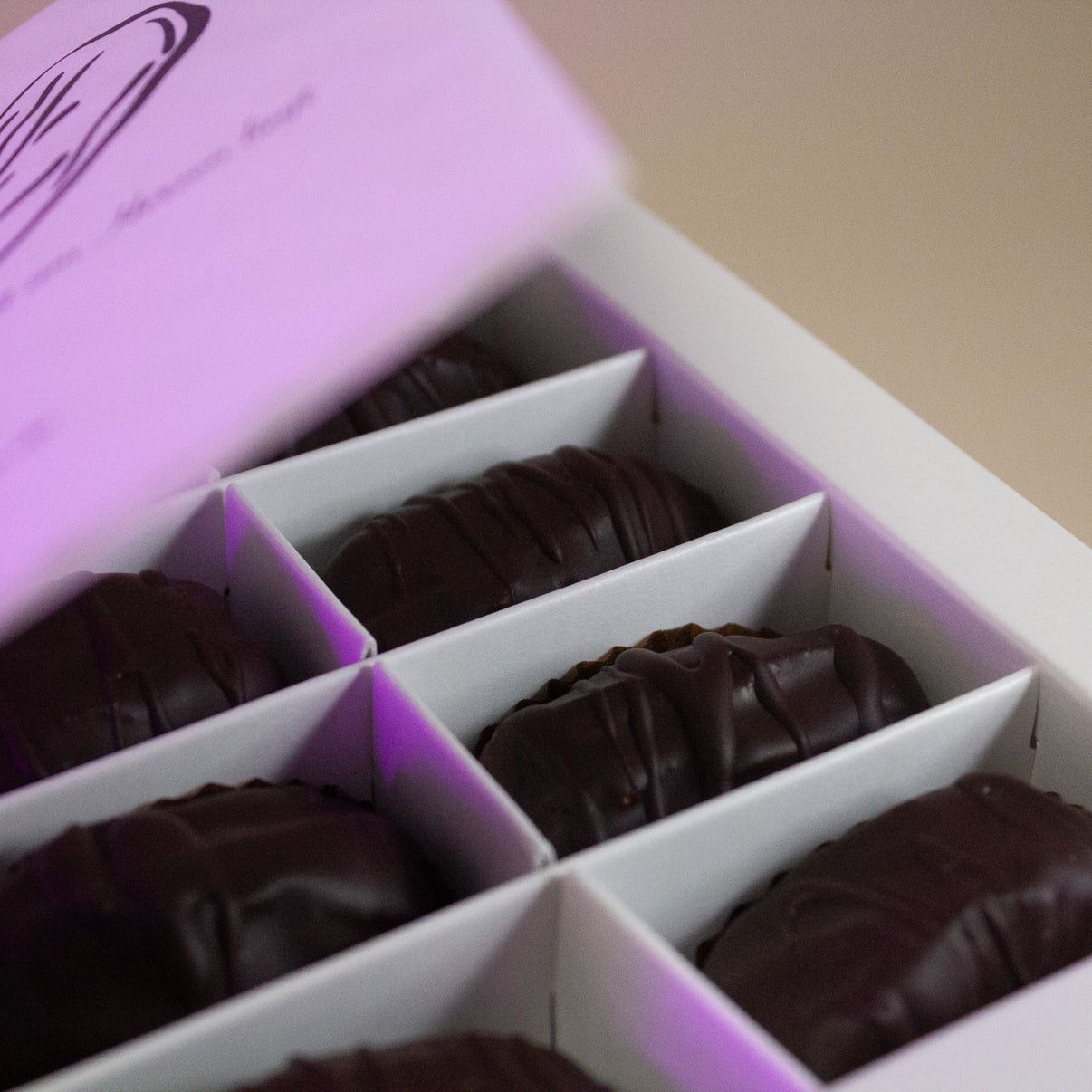 Gros plan de six dattes enrobées de chocolat noir dans une boîte cadeau blanche.