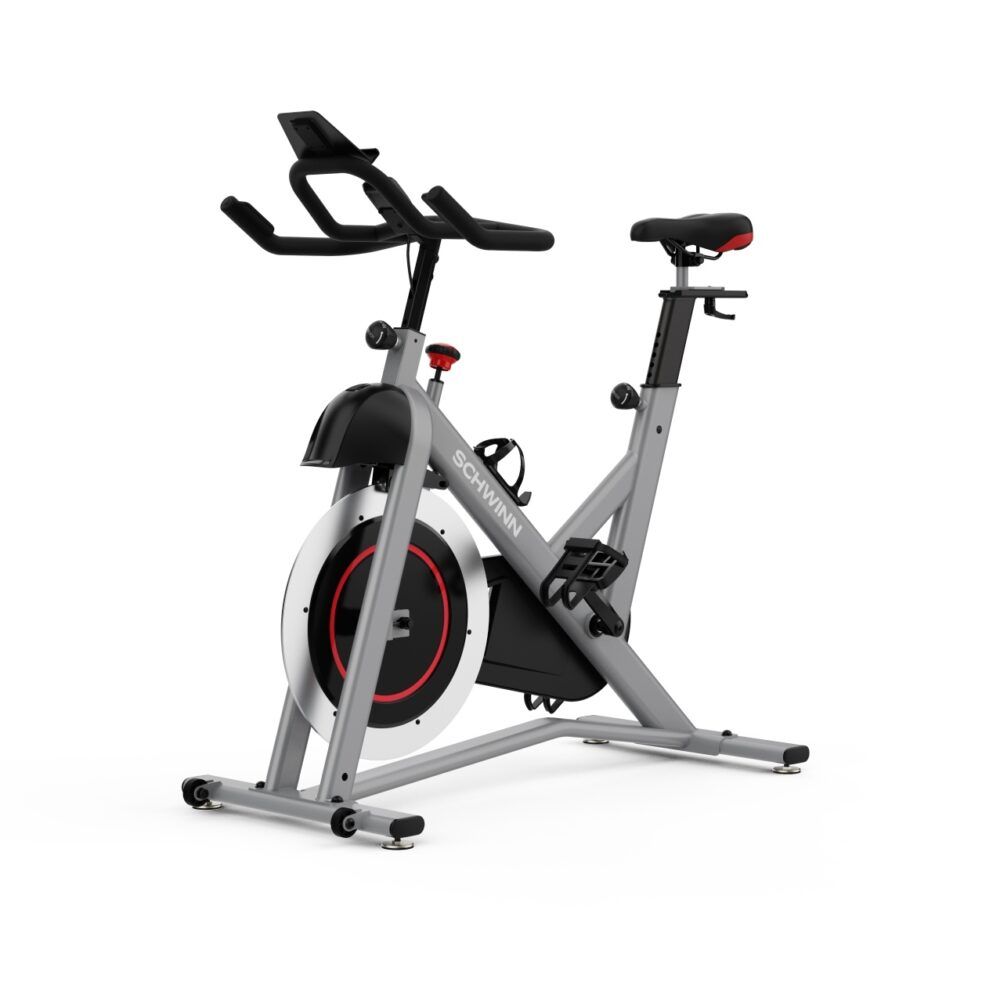 Vélo d'intérieur gris. Visible : selle, guidon, pédales, volant d'inertie. Marque : Schwinn. Accent rouge sur le volant.