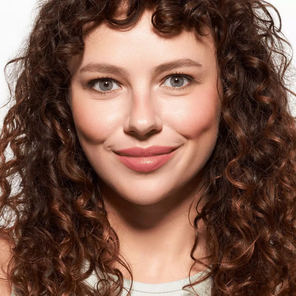 Portrait d'une femme aux cheveux bouclés. Elle sourit. Les sourcils sont mis en valeur.