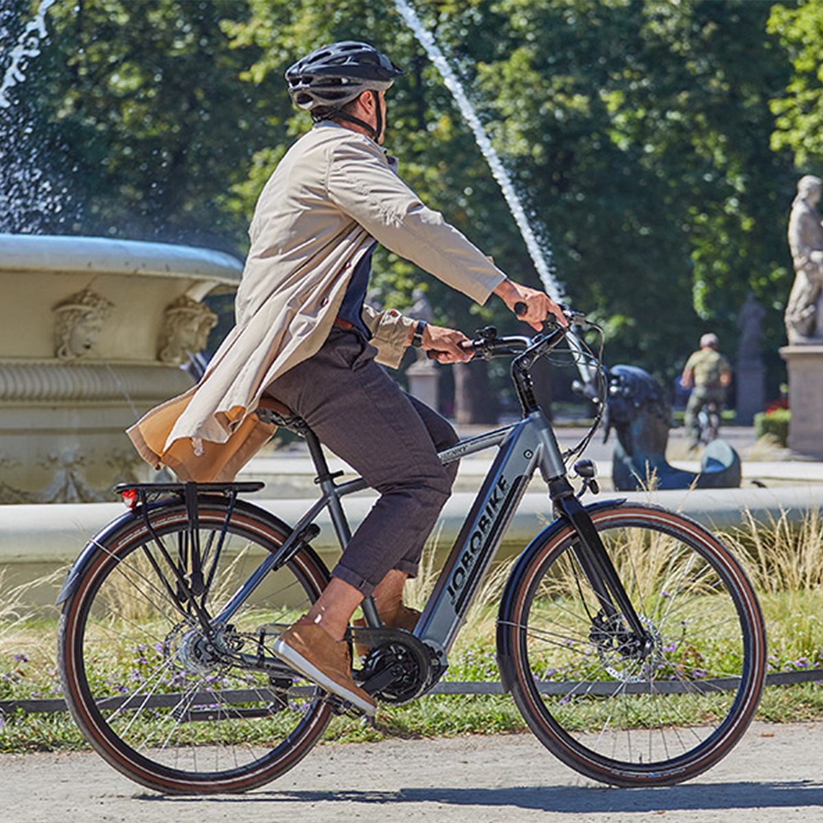 Personne faisant du vélo électrique gris dans un parc. Logo JOBOBIKE sur le cadre.