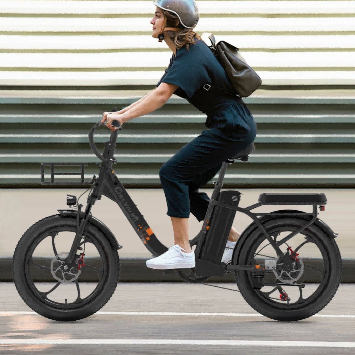 Persoon op een zwarte elektrische fiets. Draagt helm en rugzak. Achtergrond: gebouw met horizontale strepen.